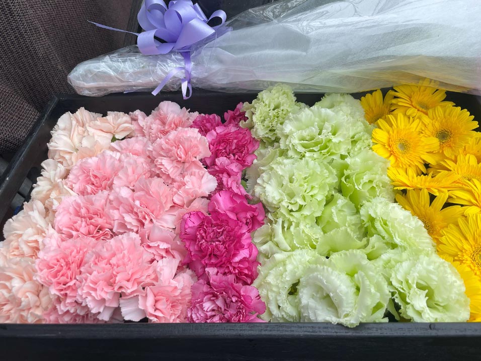 白、ピンク、黄色の花が詰められたトレーと、花束があります